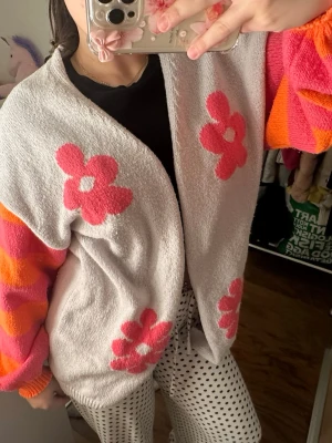 Grå kofta med blommor och färgglada ärmar - Fin cardigan med mönster, väldigt mysig och gosig perfekt att sätta på sig under en kall dag. vet ej vart ifrån eller storlek. Skulle säga S/M. Nopprig,!!