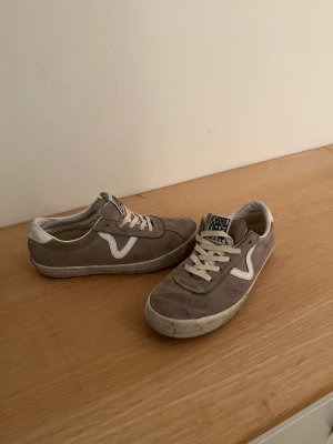 Gråa Vans sneakers i mocka OFF The Wall  - Säljer ett par gråa Vans sneakers i mocka med vit sula och vita detaljer. Klassisk Vans-logga på sidan och tung etikett med 'Off The Wall'. Skorna har snörning och platt sula, perfekt för en avslappnad streetstil.