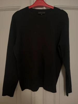 Svart stickad tröja Brand Island M - En svart stickad tröja från Brand Island i storlek M. Tröjan har rund halsringning och långa ärmar med ribbade muddar. Enkel och clean design som funkar till många olika stilar. Perfekt för dig som gillar basic och vill ha en klassisk look. 52% viskos, 20% polyamid och 28% polyester