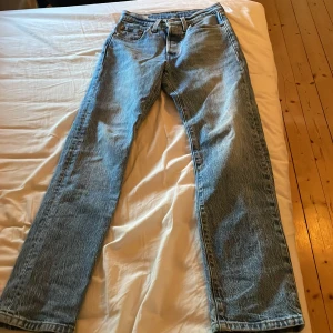 Levi's 501 blå jeans straight fit - Klassiska Levi's 501 jeans i ljusblå tvätt med rak passform och fem fickor. Jeansen har knappgylf, bälteshällor och den ikoniska röda Levi's-taggen bak. Perfekt för dig som gillar tidlös stil och vill ha ett par jeans som funkar till allt.
