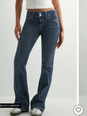 Blå bootcut jeans med broderade fickor - Snygga blå bootcut jeans med låg midja och klassisk femficksdesign. Jeansen har dubbla knappar framtill och coola broderade detaljer på bakfickorna. Tillverkade i mjukt denimtyg som sitter skönt och ger en avslappnad vibe. Jeansen är från Nelly och säljer dom för att de har blivit för små för mig. Jag är 173 cm lång.