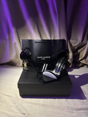 Saint Laurent klackar - Säljer ett par svarta lyxiga Saint Laurent klackar med den ikoniska ysl loggan som klack. Skorna är helt nya och kommer med lådan samt påsen som syns på bilden. Säljer dem pga dem inte passar mig. Obs. det är inte orginala ysl klackar.