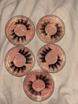 Fem par fluffiga lösögonfransar - Säljer fem par svarta, dramatiska lösögonfransar med fyllig och fluffig look. Fransarna kommer i runda plastförpackningar med glittrig rosa bakgrund. Perfekt för dig som vill ha extra volym och längd på fransarna. Materialet är syntetiskt.