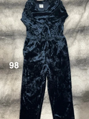 Mörkblå sammets byxdress barn - Säljer en mjuk och glansig mörkblå byxdress i sammet för barn. Byxdressen har resår i midjan och tryckknappar vid axeln för enkel påklädning. Perfekt för dig som gillar en chill och snygg look.🌸 Använd en gång. Storlek 98. 