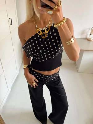 Svart prickig oneshoulder - Säljer en svart oneshoulder från Design By Si med vita prickar och croppad passform. Toppen har snörning i ryggen och är tillverkad i ett stretchigt material med ribbad midja. Perfekt för dig som vill sticka ut med en cool och trendig look. Är i storlek xs/s och har använts fåtal gånger.