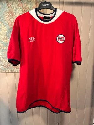Norge Umbro 2000/02 shirt, storlek XL - Skick 7,5/10.  Röd fotbollströja med Norges flagga på bröstet och Umbro logga. Tröjan har en vit och marinblå krage och detaljer på ärmarna och nederkanten.  #norway #euro #carew