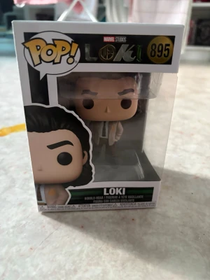 Loki från Funko Pop - Säljer en beige väst inspirerad av Loki från Marvel-serien, med klassisk krage och knappar framtill. Västen har en enkel, rak passform och är tillverkad i ett syntetmaterial. Perfekt för dig som vill sticka ut med en ikonisk look. Lådan är lite skadad 