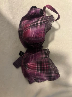 Lila rutig bh från Cleo by Panache - Säljer en snygg lila bh från Cleo by Panache med rutigt mönster och spetsdetaljer upptill på kuporna. Bh:n har en liten rosett framtill och justerbara axelband. Perfekt för dig som gillar färg och mönster!