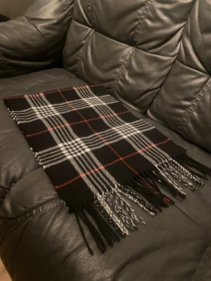 Burberry Halsduk - Jag säljer en Burberry halsduk i färgen svart med vita och röda ränder på. Den är helt ny säljer den för ingen användning. Priset är inte hugget i sten.