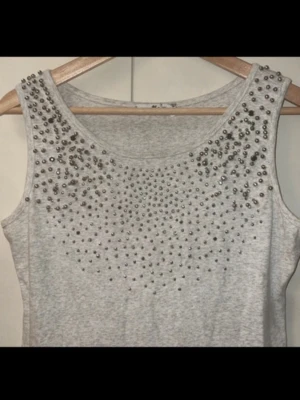 Grå ärmlös klänning - Snygg grå ärmlös kortklänning med silvriga detaljer upptill. Klänningen har en rak passform och är gjord i mjukt bomullsmaterial. Perfekt för dig som gillar en enkel men ändå edgy stil.