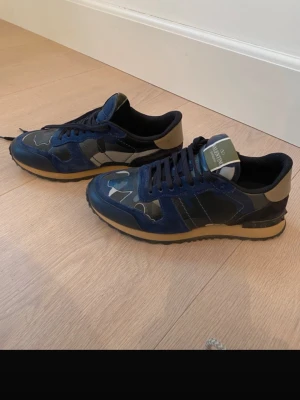 Valentino Rockrunner - Snygga Valentino Rockrunner sneakers i blått och svart med camouflage-mönster. Skorna har detaljer i mocka och skinn, svarta snören och beige sula. Perfekta för dig som vill sticka ut med stil. Storlek 40,5 men passar en storlek större. Skorna är i väldigt fint skick! skinnet och mocka detaljerna är superfina. Endast några små repor på tån som knappt syns. Endast skorna följer med. Bara att höra av sig vid frågor eller liknande! Priset kan självklart diskuteras.