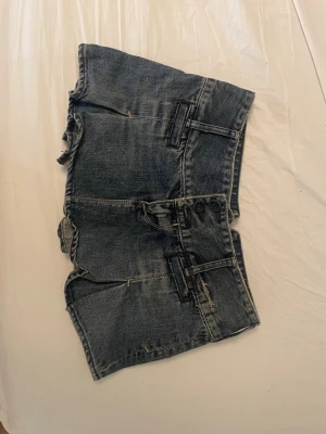 Jeanskjol från Abercrombie - Kort jeanskjol från Abercrombie i mörkblå denim med slitna detaljer och volangkant. Kjolen har bälteshällor, dekorativa fickor och knappdetaljer fram och bak. Den passar tyvärr inte mig så därför säljer jag den😊
