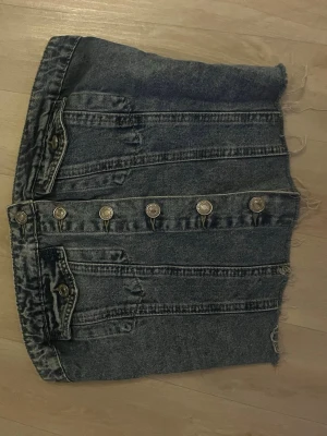 Mörkblå croppad jeans tubtopp - Säljer en croppad tubtopp i mörkblå denim med knappar framtill och råa kanter. Toppen har dekorativa fickor och en cool vintagekänsla. Perfekt för dig som vill sticka ut med en unik jeanslook.