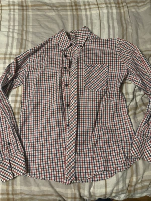 Rutig skjorta från Ben Sherman M - Säljer en klassisk rutig skjorta från Ben Sherman i storlek M. Skjortan har röda, blå och vita rutor, lång ärm, bröstficka och knappar framtill. Perfekt för dig som gillar en tidlös och clean stil.