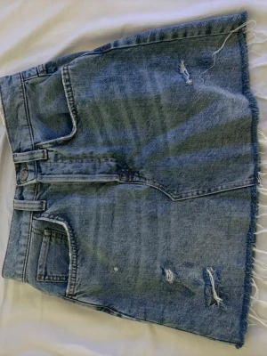 Blå jeanskjol från BikBok XS - Säljer en blå jeanskjol från BikBok i storlek XS. Kjolen är kort, har slitna detaljer och fransig nederkant för en avslappnad vibe. Klassisk femficksmodell med knappar framtill. Perfekt till sneakers eller boots.