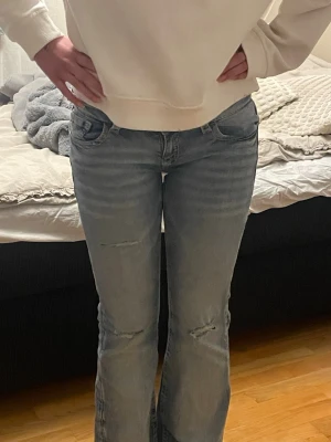 Ljusblå bootcut jeans med broderade fickor - Säljer ett par ljusblå bootcut jeans med slitningar på benen och snygga broderade bakfickor med lock och knapp. Jeansen har normal passform och är lågmidjade. Dom är jätte fina och använda ca 3 gånger. Säljer då dom inte kommer till användning. Jag på bilden är 170 ungefär och de passar bra. Innerbenslämgden är 79cm och midjemåttet är 38