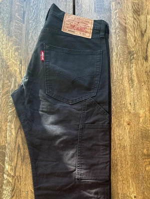 Svarta Levi's cargopants - Svarta cargopants från Levi's med raka ben och flera praktiska fickor på sidorna. Klassisk röd Levi's-tag bak och patch i läder i midjan. 