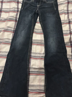 Blå bootcut jeans från Gina Tricot - Säljer ett par mörkblå bootcut jeans från Gina Tricot i storlek 146. Jeansen har kontrastsömmar och bakfickor med broderade detaljer och paljetter i guldton. Klassisk femficksmodell i jeansmaterial med snygg tvätt och markerade sömmar.