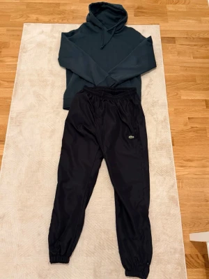 Outfit 1# enkel grön hoodie med nylon Lacoste byxor L  - En enkel outfit man kan ha på sig under sin vardag för ett schysst och bra pris. Nytt skick på byxorna och tröjan lite använd, storlek —> L