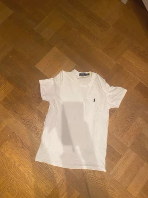Vit t-shirt från Polo Ralph Lauren - Klassisk vit t-shirt från Polo Ralph Lauren med soprent snitt och den ikoniska broderade loggan på bröstet. Tillverkad i mjuk bomull och har normal passform med korta ärmar. Perfekt till jeans eller shorts för en clean look.