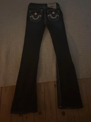 Blåa bootcut jeans med kontrastsömmar - Säljer ett par blåa  jeans med tydliga vita kontrastsömmar och snygga detaljer på bakfickorna. Byxorna har bootcut-modell och låg midja, vilket ger en retrovibe. Materialet är klassisk jeans och passformen är normal. Perfekta för dig som vill sticka ut lite extra! Kostar 2400 i nypris