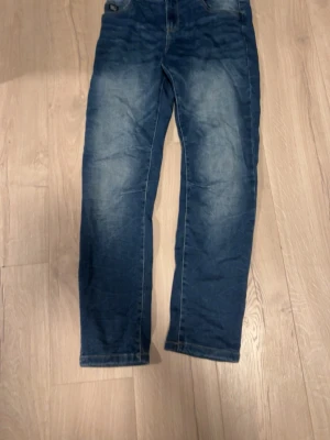 Jeans från lab industries  - Säljer ett par klassiska blå jeans från LAB Industries i storlek 170. Jeansen har en rak passform med snyggt slitna detaljer och kontrastsömmar. Tillverkade i hållbar denim och har fem fickor samt bälteshällor. Perfekta för en avslappnad och stilren look.