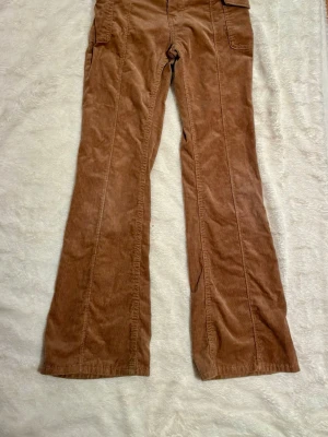 Bruna manchesterbyxor från Lindex - Säljer ett par bruna manchesterbyxor från Lindex i storlek 146. Byxorna har bootcut-ben, fickor på sidorna och justerbar midja med knappresår. Perfekta för dig som gillar retrovibbar och mjukt material.