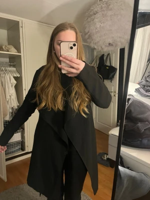 Svart kappa från ONLY med bälte - Säljer en svart kappa från ONLY i storlek M. Kappan har en snygg omlott-design och knyts med bälte i midjan. Den är lång och har långa ärmar, perfekt för dig som gillar en stilren och enkel look. Materialet är lite tunnare så bättre till höst/vår.