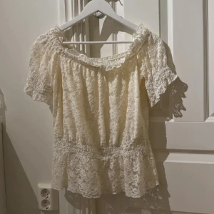 Offshoulder spetsblus från Bodyflirt - Offshoulder blus i cremevitt från Bodyflirt. Blusen är täckt av vacker spets, har korta ärmar och volangkant nertill. 💞