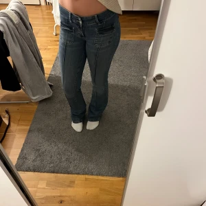 Blå bootcut jeans från Nelly, stl 36 - Snygga blå bootcut jeans från Nelly med stora fickor framtill och klassisk femficksdesign. Jeansen har normal passform och är tillverkade i ett mjukt bomullsmaterial med lite stretch. Perfekta för dig som gillar en retroinspirerad look.
