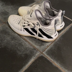 Adidas Stabil vita inomhusskor.✨ - Säljer ett par Adidas Stabil inomhusskor i vitt med svarta detaljer och grå inslag. Skorna har klassiska tre ränder på sidan, snörning och en ljus gummisula. Ovandelen är i syntetmaterial och mesh för bra andningsförmåga. Perfekta för inomhussport eller träning. | För mer frågor och funderingar skriv till mig.✨
