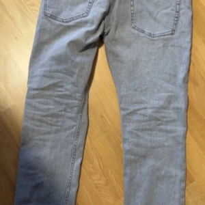 Ljusgrå raka jeans - Säljer ett par ljusgrå jeans med raka ben och klassiska bakfickor. Jeansen har en enkel design utan synliga detaljer och är tillverkade i mjukt denimtyg. Perfekta för dig som gillar en clean och stilren look.