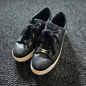 Svarta sneakers med platåsula - Svarta sneakers med vit platåsula och snörning. Skorna har rund tå, silverfärgade öljetter och breda svarta skosnören. Tillverkade i syntetmaterial med en stilren och enkel design som passar till många outfits.