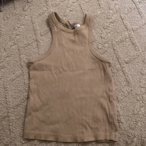 Beige ribbad linnetopp från h&m. - Säljer en beige ribbad linnetopp från h&m. Toppen har en klassisk rak passform med breda axelband och ärmlös design. Materialet är mjuk bomull med stretch och ribbad struktur som ger en snygg och enkel look. Aldrig använd bara prislappen som togs bort 