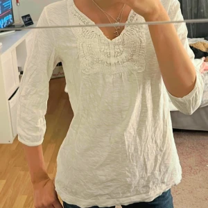 Vit blus med spets från Esprit - Vit blus från Esprit med v-ringning och vacker virkad spetsdetalj framtill. Blusen har trekvartsärm och är tillverkad i mjuk bomull, perfekt för en avslappnad men ändå stilren look💕