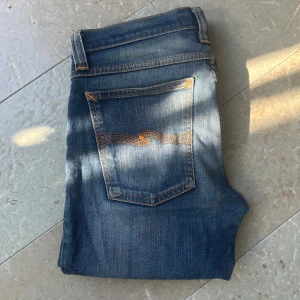 Nudie jeans  - Säljer ett par klassiska blå jeans från Nudie Jeans med snyggt slitna detaljer och kontrastsömmar. Skick:9/10 w30 L29