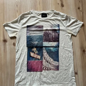 Vit t-shirt från Vailent Strl M - Säljer en vit t-shirt från Vailent i storlek M med coolt grafiskt tryck på framsidan i blått, lila och beige toner. T-shirten har rund hals och korta ärmar, tillverkad i mjuk bomull. Perfekt för dig som gillar streetstyle och unika prints.