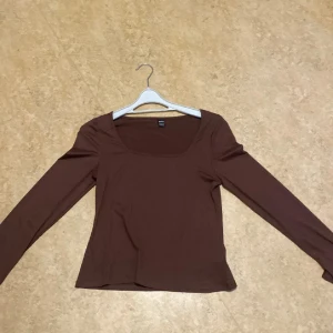 Brun långärmad topp från SHEIN - Säljer en brun långärmad topp från SHEIN i storlek L. Toppen har en snygg fyrkantig urringning och är figurnära i modellen. Materialet känns mjukt och stretchigt, perfekt att styla med jeans eller kjol för en clean look.