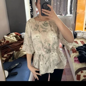 Blommig blus från Stockh LM - Säljer en superfin blommig blus från Stockh LM i ljusbeige med gröna och vita blommönster. Blusen har trekvartsärmar, rund halsringning och en lätt volang nertill som ger en snygg siluett. Perfekt för vår och sommar!