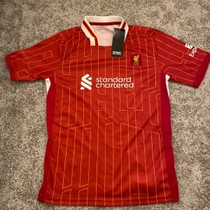 Fotbollströja med shorts LIVERPOOL LFC - Fotbolls tröja med shorts. Väldigt luftigt material och perfekt för varma dagar eller till träning, helt nya aldrig använda. Perfekt att ha som julklapp eller till personligt bruk! MVH