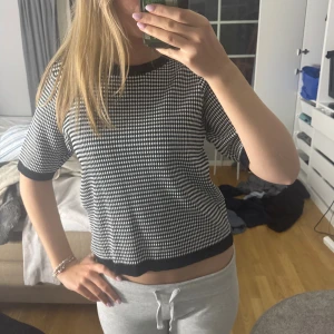 Svartvit mönstrad stickad tröja - ENDAST ANVÄND EN GÅNG! Säljer en svartvit stickad tröja från Pernilla Wahlgrens märke  med kort ärm och rund hals. Tröjan har ett tätt, rutigt mönster och svarta ribbade kanter vid hals, ärmslut och nederkant. Liten guldfärgad Pineapple-detalj nertill. Perfekt till både jeans och kjol! 