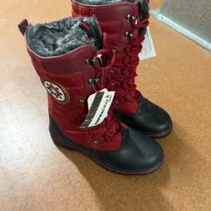 Röda vinterstövlar med fuskpälsfoder - Snygga röda vinterstövlar från Supracor med svart tå och sula, snörning framtill och grått fuskpälsfoder. Stövlarna har broderad snöflinga på sidan och detaljer i syntetmaterial. Perfekta för kalla dagar när du vill hålla stilen och värmen.