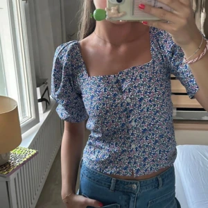 Blus  - Supersöt blommig blus med kort puffärm och fyrkantig ringning. 