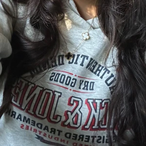 Grå hoodie från Jack & Jones - Säljer en ljusgrå hoodie från Jack & Jones med tryck i rött, blått och svart framtill. Tröjan har huva och en stor magficka. Perfekt för dig som gillar en avslappnad och sportig stil.