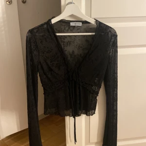 Svart mesh blus från Venderby's XS/S - Säljer en svart spets blus från Venderby's i storlek XS/S. Blusen har lång ärm, v-ringning och snörning framtill. Den är genomskinlig med blommigt mönster och volangdetaljer vid midjan och nederkant. Perfekt för dig som gillar trendiga och detaljerade toppar. Endast användt denna en gång, nypris ca 500kr.
