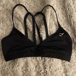 Svart bikiniöverdel från Gymshark XS - Mörkblå sport-bh från Gymshark med coola dubbla axelband i ryggen och stilren logga framtill. Tillverkad i återvunnen polyester och elastan.