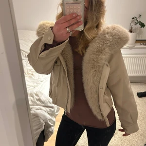 Beige fluffjacka i fuskläder - (bild 3 är lånad!) Supersöt jacka i beige fuskläder och fluffig päls runt huvan och framkanten, samt lite croppad passform. Pälsen är avtagbar. Jackan är helt ny med lappen kvar, aldrig använd.  Storlek S, passar bra på XS oxå! Perfekt till höst och vinter. Hör av er vid frågor💞💞