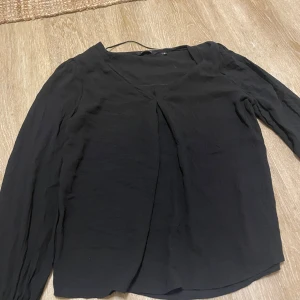 Svart blus med v-ringning Amelie & Me - Svart blus från Amelie & Me i storlek S. Blusen har v-ringad hals, långa ärmar med breda, ribbade muddar och ett lätt, flowigt tyg. Perfekt för dig som gillar stilrena och enkla plagg med snygga detaljer.