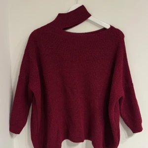 Vinröd stickad tröja med hög krage - Vinröd stickad tröja med unik hög krage och avslappnad passform. Tröjan har långa ärmar och är tillverkad i en mjuk blandning av ull och akryl. Perfekt för dig som gillar en lite loose och cozy stil.