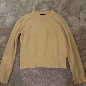 Ljusgul stickad tröja från KappAhl - Säljer en ljusgul stickad tröja från KappAhl i storlek S. Tröjan har en rund halsringning, ribbade muddar och långärmade ärmar. Perfekt för dig som gillar mjuka och mysiga plagg med enkel design och snygg passform.